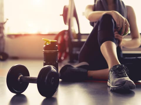 Frau sitzt erschöpft im Fitnessstudio