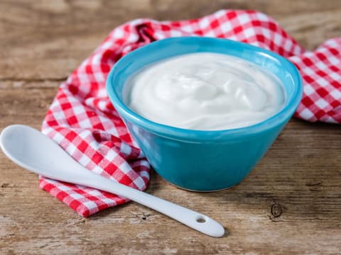 Joghurt in Schüssel auf kariertem Tuch auf Tisch