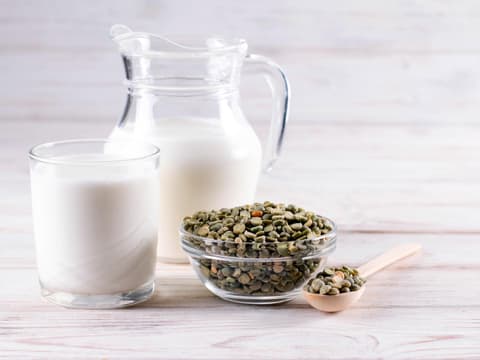 Milchglas und Karaffe mit trocknen, grünen Erbsen davor