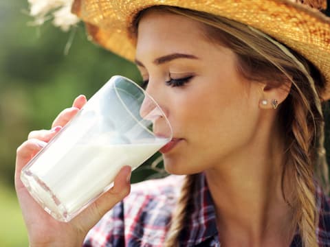 Frau mit Hut trinkt Milch aus Glas