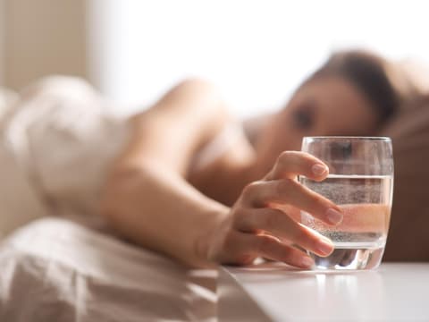 Frau trinkt Wasser im Bett