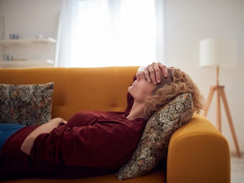 Frau mit Kopfschmerzen liegt auf Sofa