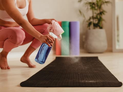 Frau Reinigung Übungsmatte mit Desinfektionsspray in Fitness-Studio