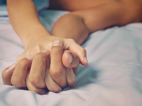 Zwei ineinander verwobene Hände im Bett