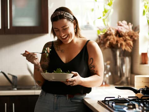 glückliche Frau mit Tattoos isst Salat