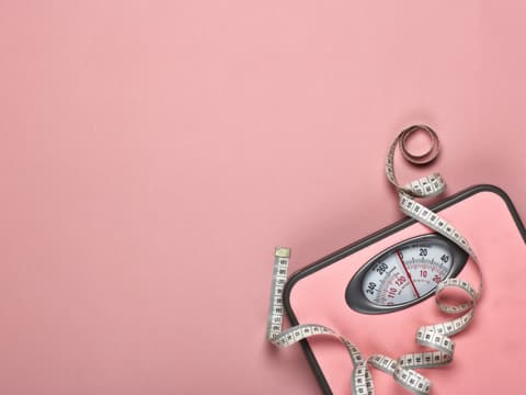 Pinke Waage mit Maßband vor pinkem Hintergrund