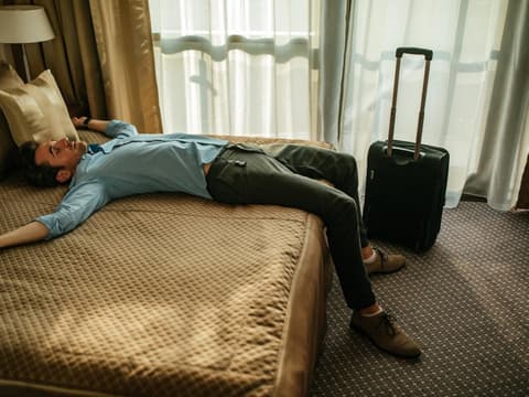 Mann liegt erschöpft auf Hotelbett