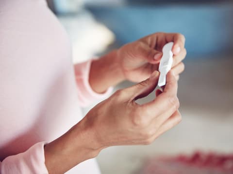 Frau hält Schwangerschaftstest in den Haenden