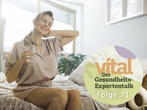 Reife Frau sitzt mit Glas Wasser im Bett