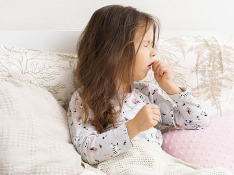 Mädchen liegt im Bett und hustet