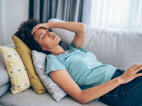 Frau liegt mit verschleppter Lungenentzündung auf dem Sofa und zeigt Symptome