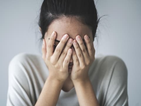 Junge Frau mit Moebius Syndrom schlägt Hände vors Gesicht