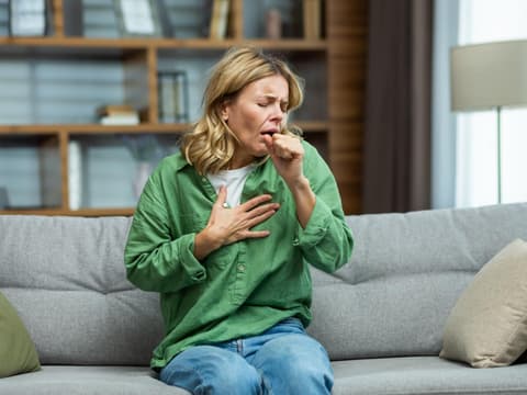 Frau sitzt auf dem Sofa und hustet