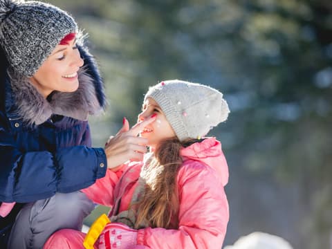 Frau trägt Wettercreme auf Gesicht eines Kindes auf