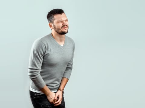 Mann fasst sich mit schmerzverzerrtem Gesicht zwischen die Beine
