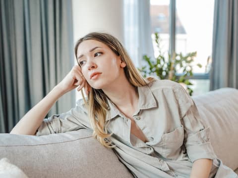 Frau sitzt auf Sofa und guckt traurig