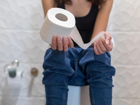 Frau sitzt auf Toilette mit Toilettenpapier in der Hand