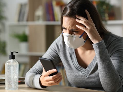 Frau trägt eine Maske und guckt besorgt auf ihr Handy