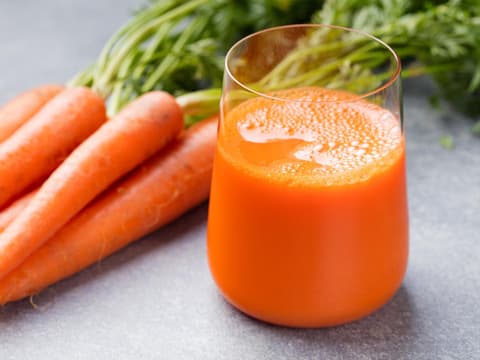 Ein Glas frisch gepresster Karottensaft mit einem Bündel Karotten daneben