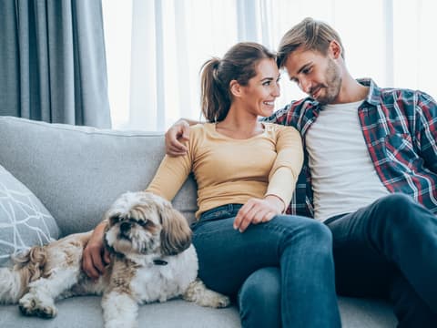 Ein glückliches Paar sitzt zusammen mit ihrem Hund auf der Couch