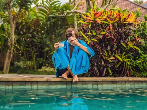 Mann sitzt im Urlaub mit Erkältung am Pool