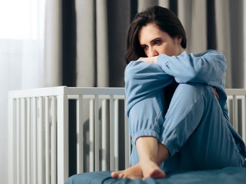 Eine traurige Frau sitzt vor einem leeren Kinderbettchen