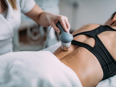 Physiotherapeutin behandelt den Rücken einer Patientin mit einem Ultraschallgerät.