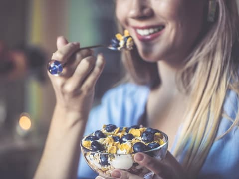 Frau mit schönen Zähnen isst einen Löffel Müsli mit Joghurt 