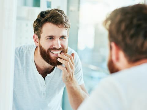 Mann bewundert seine gesunden Zähne im Spiegel