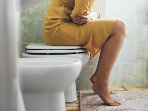 Frau sitzt auf Toilette und hält sich den Bauch