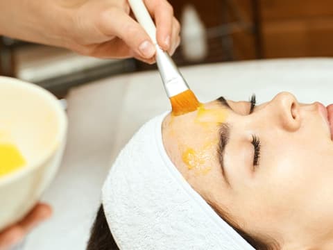 Frau bekommt ein Peeling auf das Gesicht aufgetragen