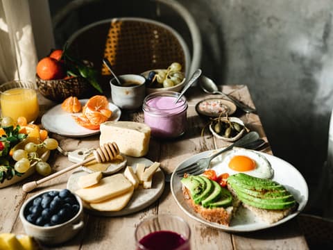 Bunt gedeckter Frühstückstisch mit Käse, Obst, Joghurt und Avocado-Brot mit Spiegelei