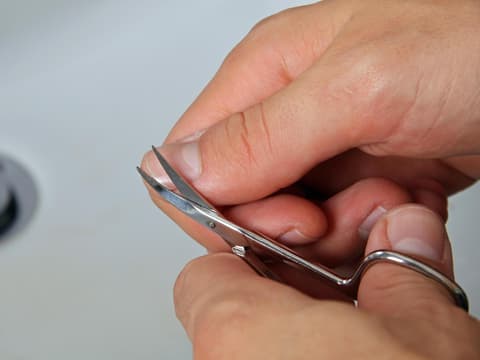 Frau schneidet sich den Daumennagel mit einer Nagelschere