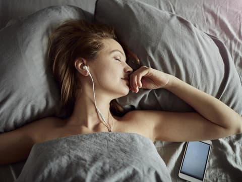 Frau liegt im Bett und hört Hörbücher zum Einschlafen