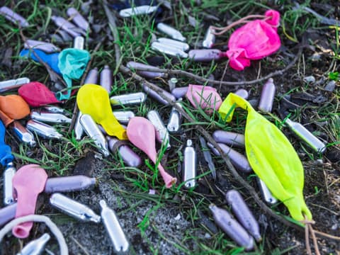 Lachgaskartuschen und leere Luftballons nach einer Party auf dem Boden