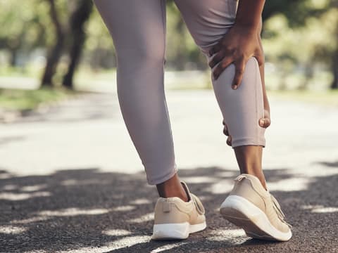 Eine Joggerin hält sich die schmerzende Wade