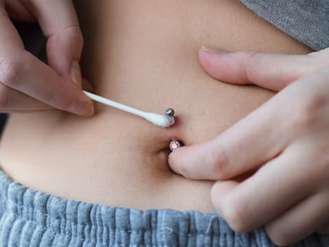 Frau pflegt ihr Bauchnabel-Piercing
