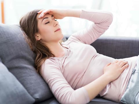 Frau liegt mit Bauchschmerzen auf dem Sofa