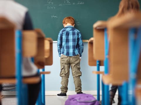 rothaariger Schuljunge steht enttäuscht vor der Tafel mit Händen in den Taschen