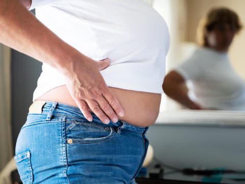 Frau guckt sich ihren Bauch im Spiegel an