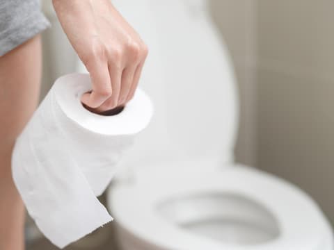 Frau steht mit Toilettenpapier in der Hand vor der Toilette