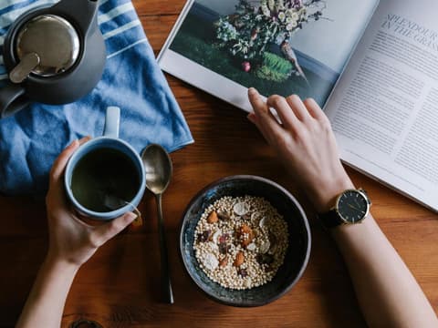 Draufsicht auf Frau am Tisch mit Magazin, Tee und Frühstücksschale