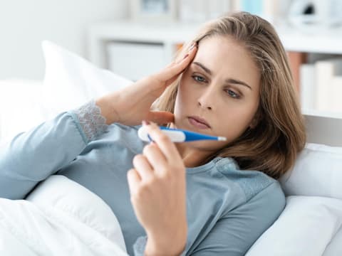 Frau schaut auf Fieberthermometer