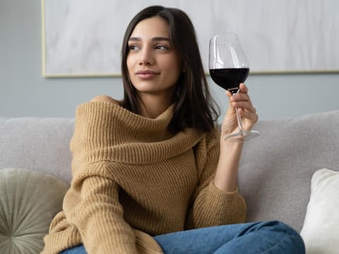 Frau sitzt mit einem Glas Rotwein auf dem Sofa