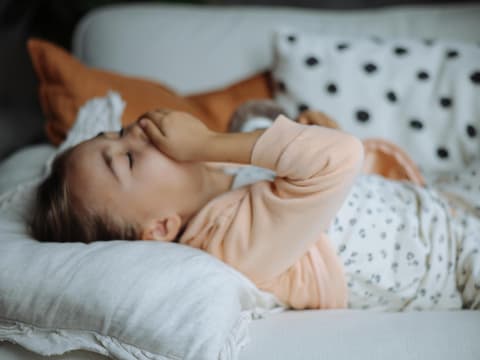 Mädchen liegt im Bett und hustet.