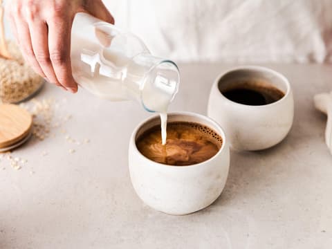 Frau gibt Milch in Kaffee