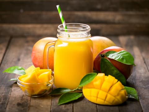 Ein Glas Mangosaft umgeben von Mangofrüchten.