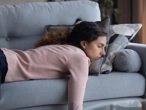 Müde Frau liegt auf dem Sofa und vergräbt Gesicht in den Kissen