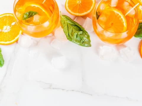 Gläser mit Orangenlimonade und Basilikum zwischen Eiswürfeln.