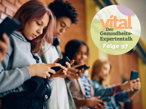Gruppe Jugendlicher steht an Backsteinwand und alle schauen auf ihre Handys